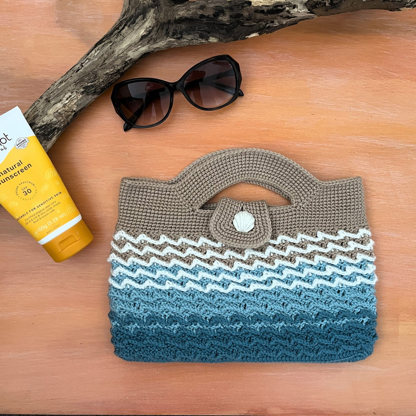 Crocheted bag with wunderbod sunscreen and sunglasses on a wooden surface