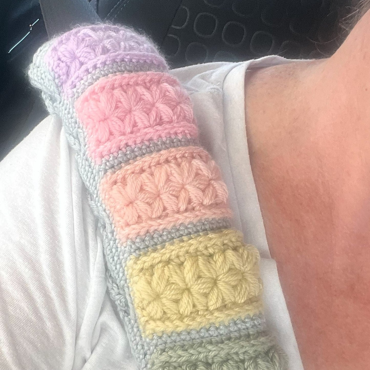 Colorful crocheted car seat cover held by a person in a vehicle.