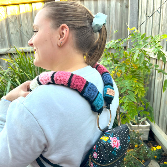Person wearing a colorful knitted item on their shoulder with a floral-patterned bag.