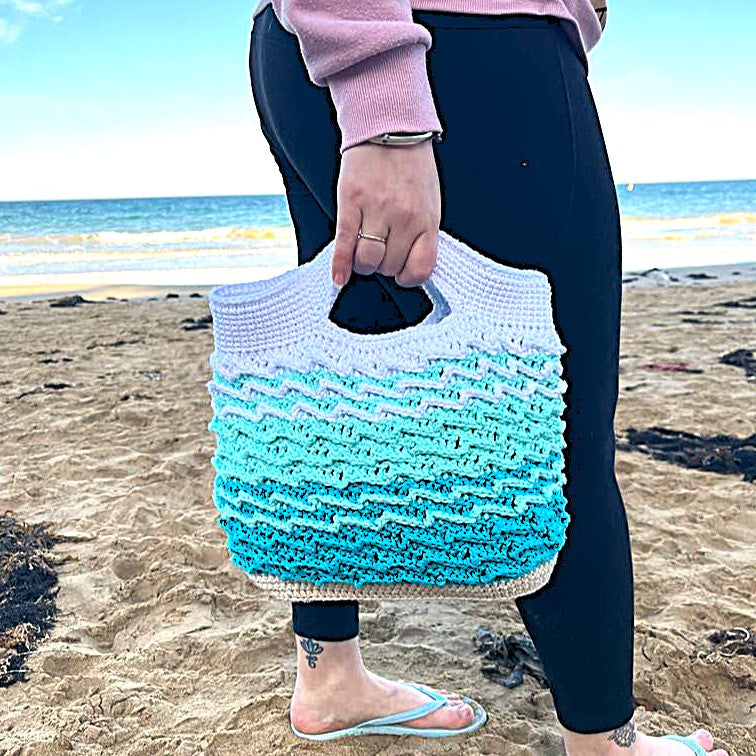 Person holding a blue and white woven bag on a beach