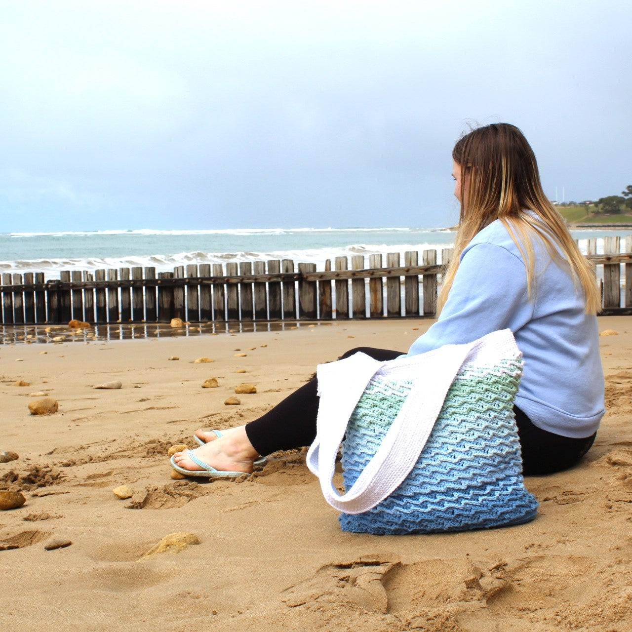 Person sitting on a beach with a blue and white crochet beach bag