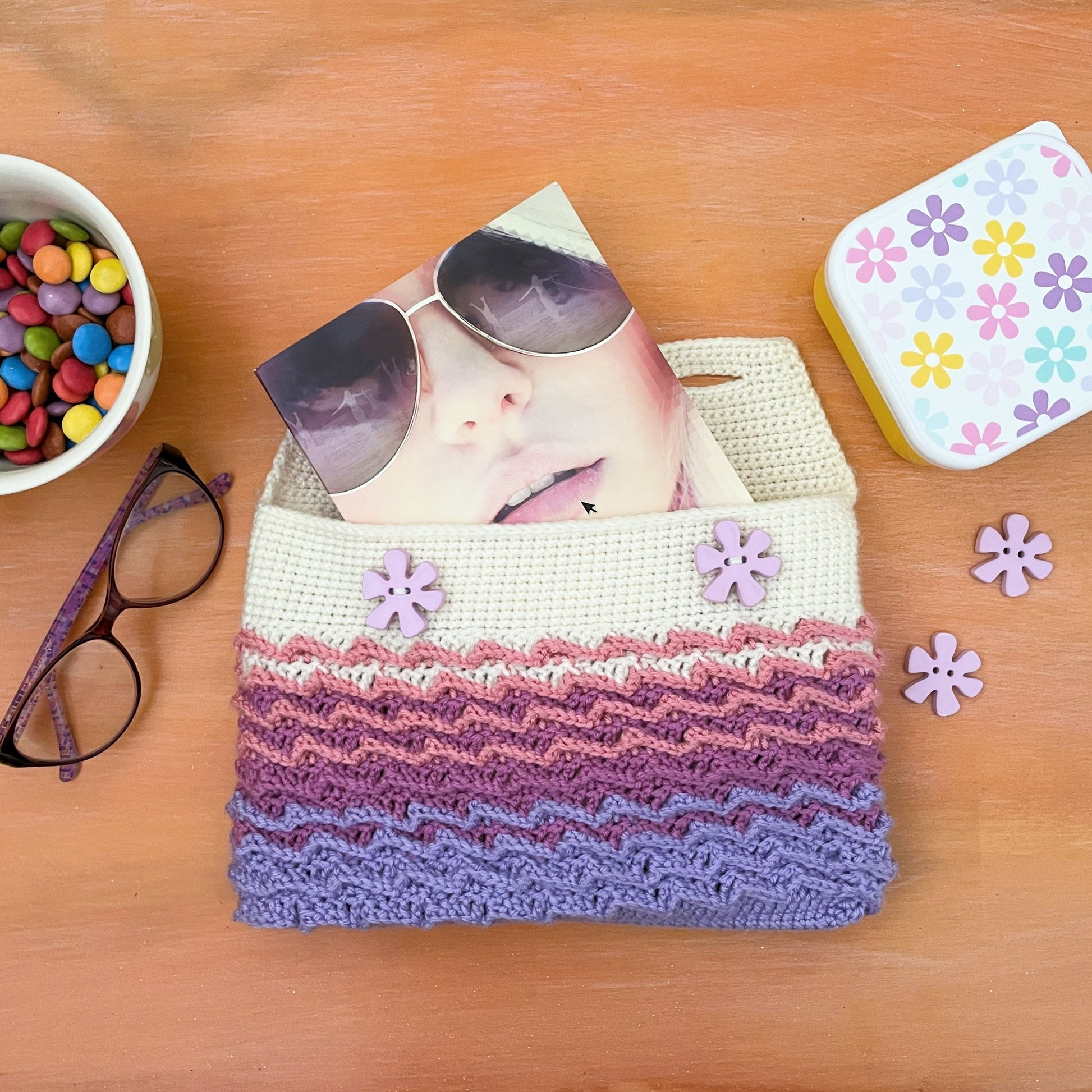 Knitted pouch with flowers, mug with candies, and sunglasses on a wooden surface