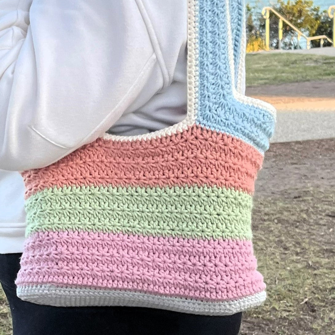 Pastel striped crochet bag worn over shoulder with outdoor background