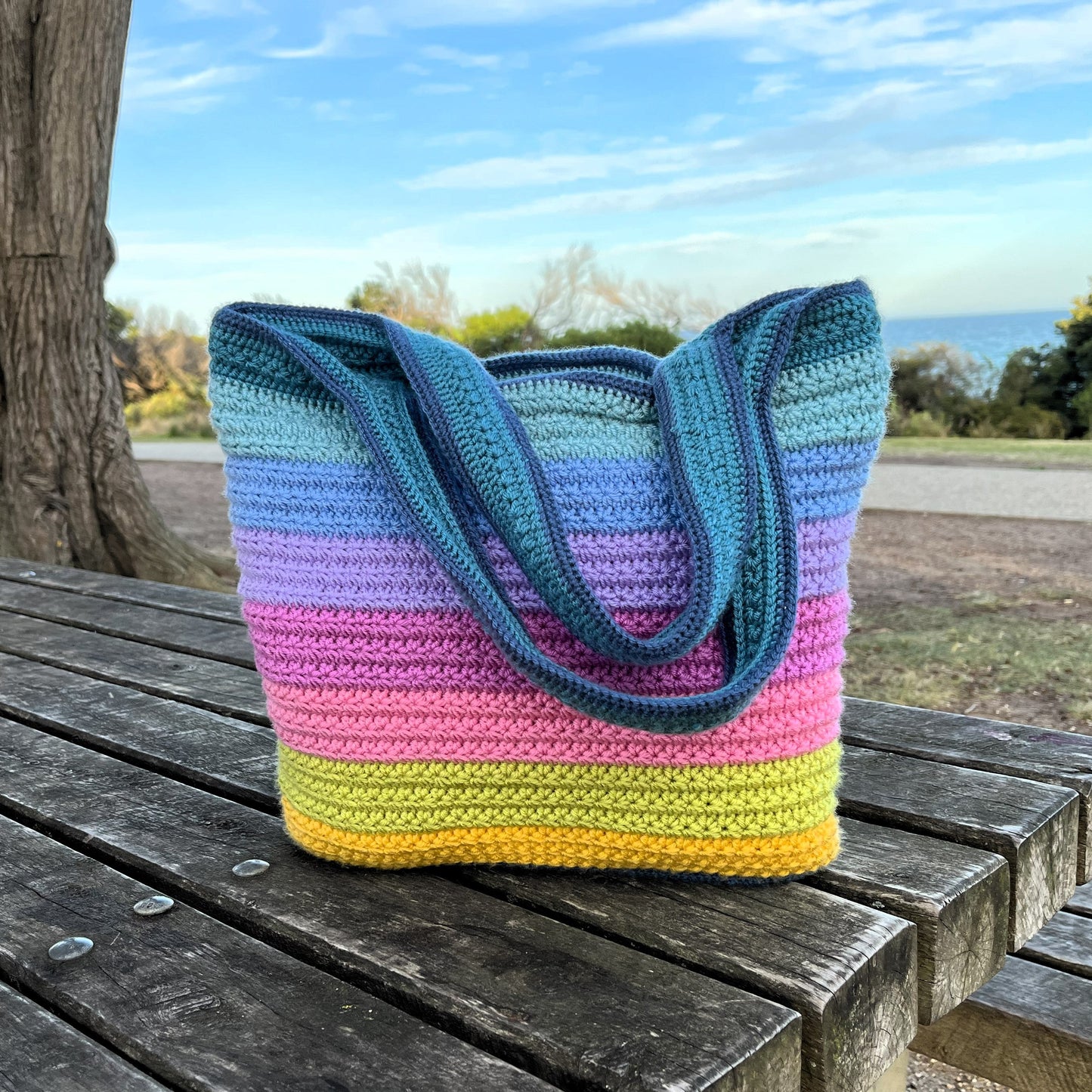 Colorful striped crochet bag on a wooden bench outdoors