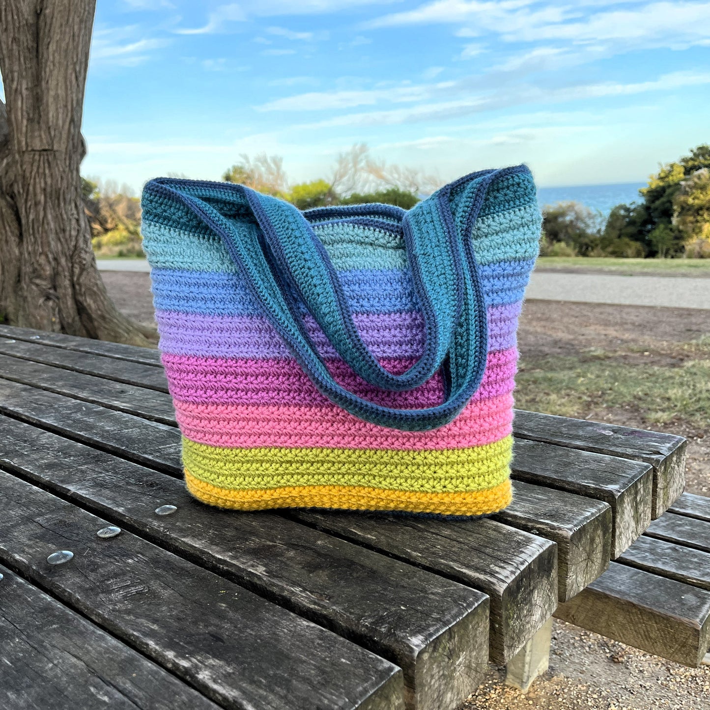 Colorful striped crochet bag on a wooden bench outdoors