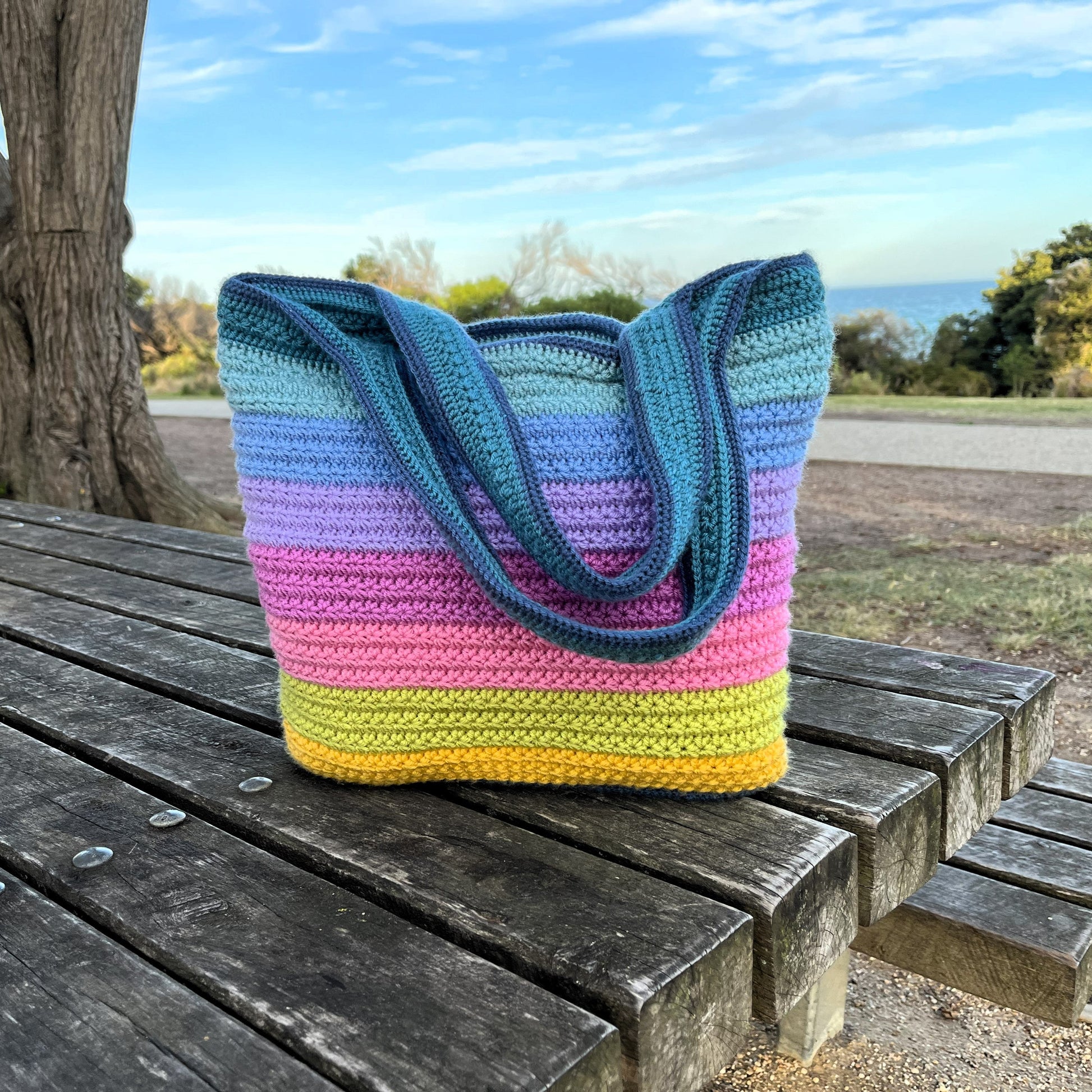 Colorful striped crochet bag on a wooden bench outdoors