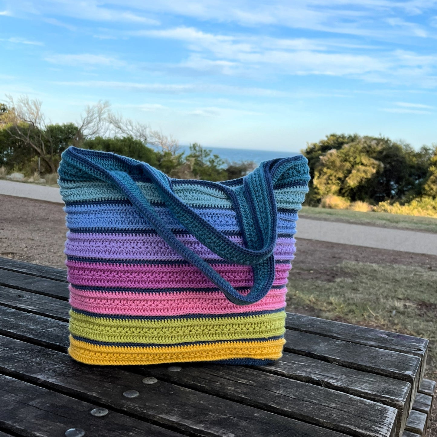 Colorful striped crochet bag on a wooden bench with a scenic background