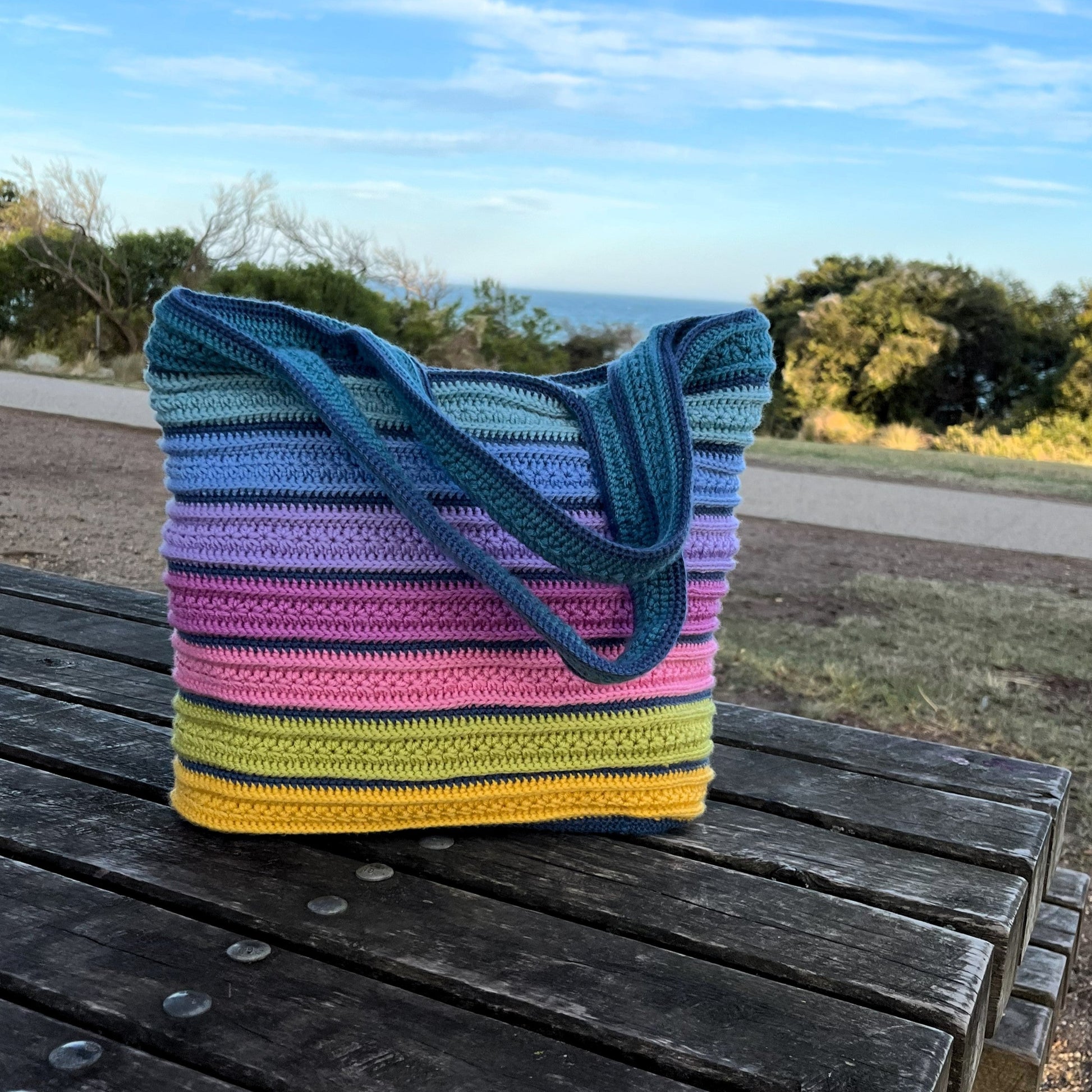 Colorful striped crochet bag on a wooden bench with a scenic background