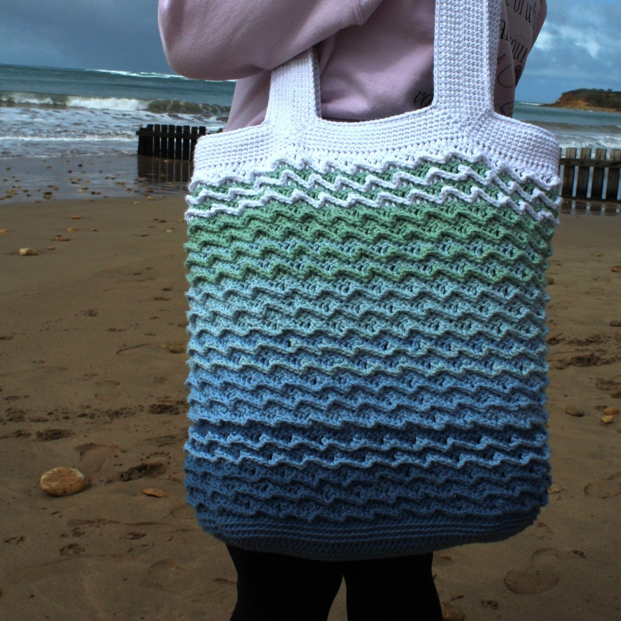 Person holding a white and green patterned tote bag on a beach