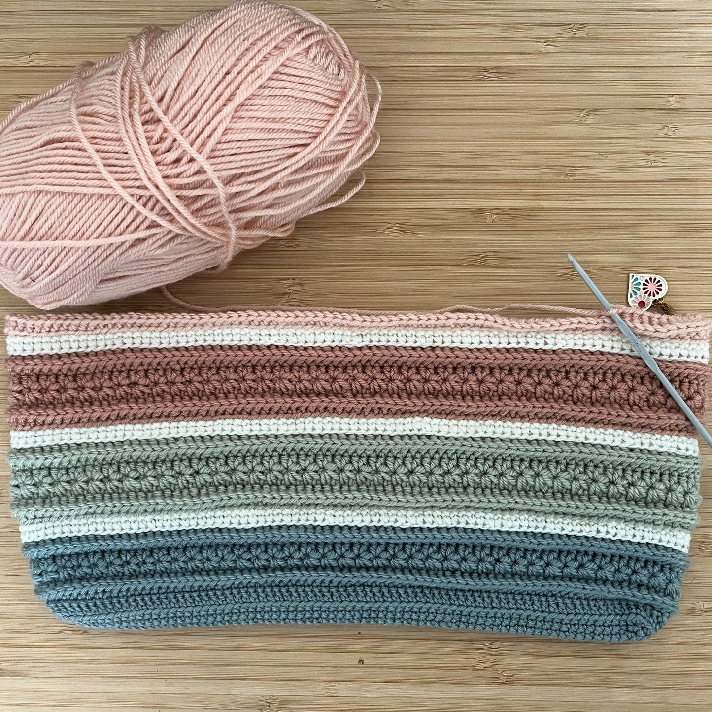 Crocheted bag with striped pattern next to a ball of yarn on a wooden surface