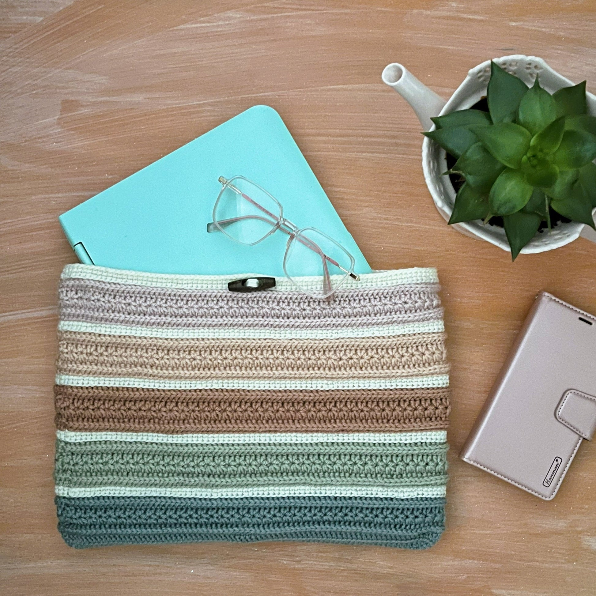 Striped pouch on a wooden surface with a notebook, glasses, and plant