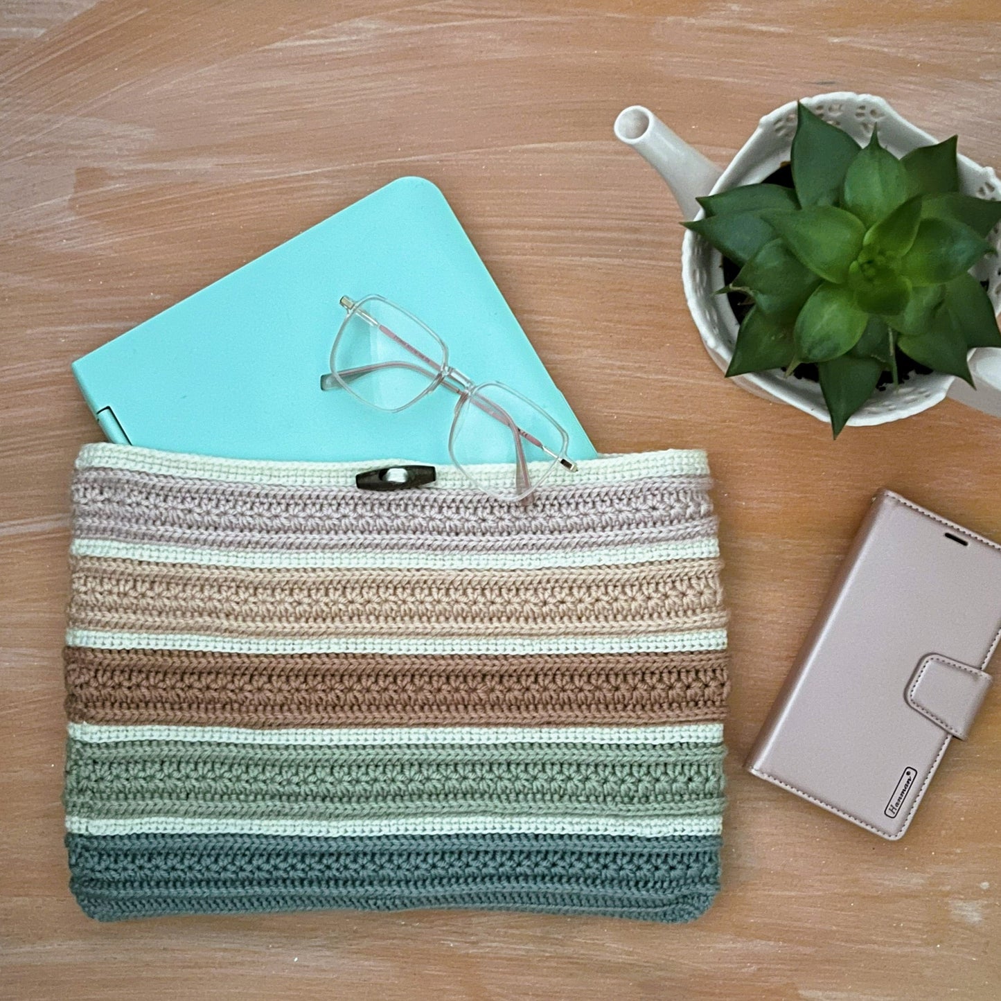 Striped pouch on a wooden surface with a notebook, glasses, and plant