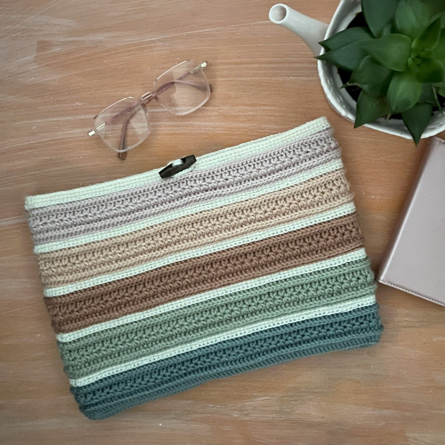 Striped pouch on a wooden surface with sunglasses, plant, and phone case.