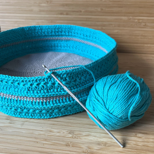 Turquoise crocheted item and yarn ball with a crochet hook on a wooden surface