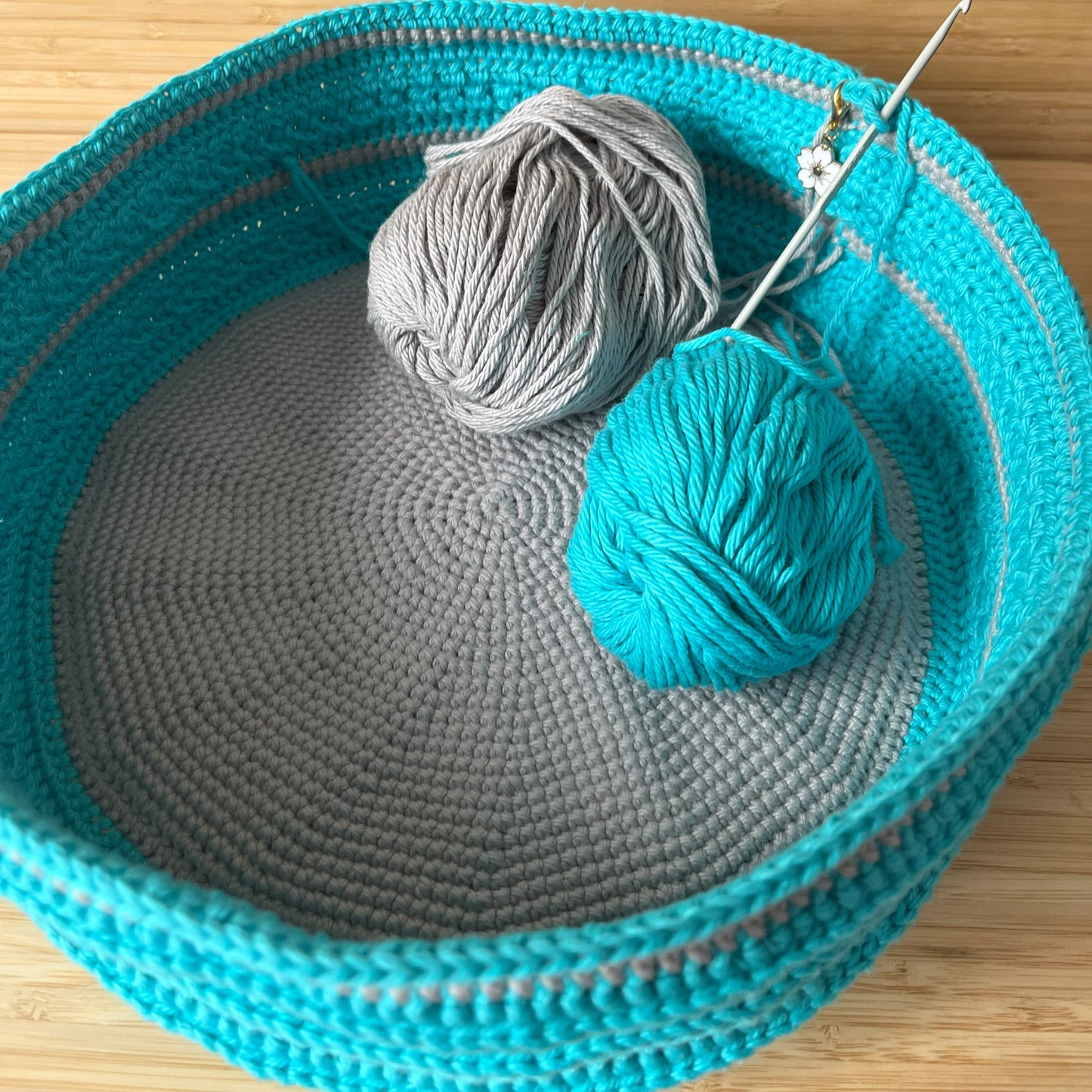 Two balls of yarn and a knitting needle in a teal woven basket on a wooden surface.