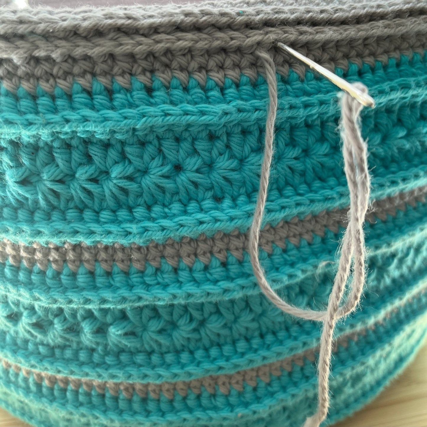 Close-up of a crocheted basket with blue and gray pattern on a wooden surface