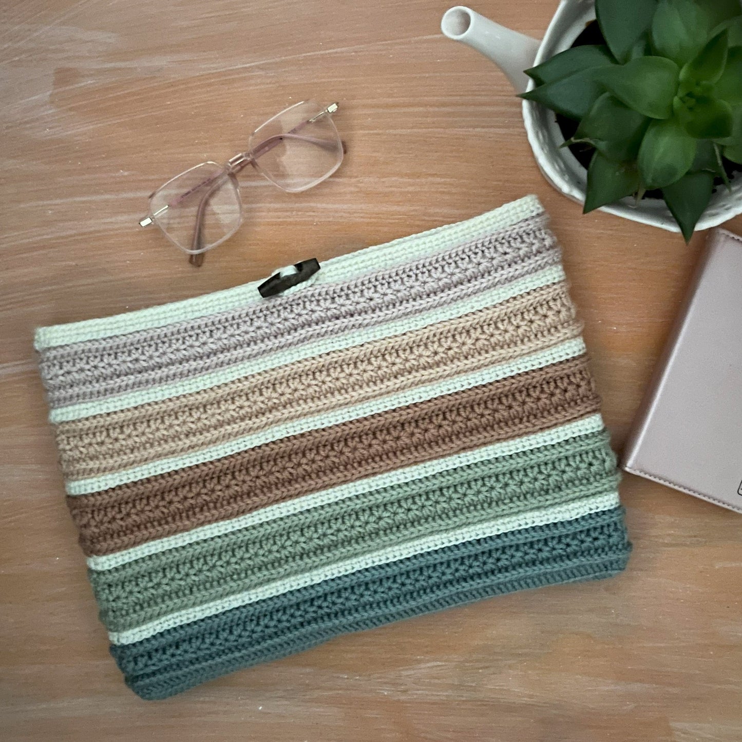 Striped pouch on a wooden surface with glasses, plant, and phone.