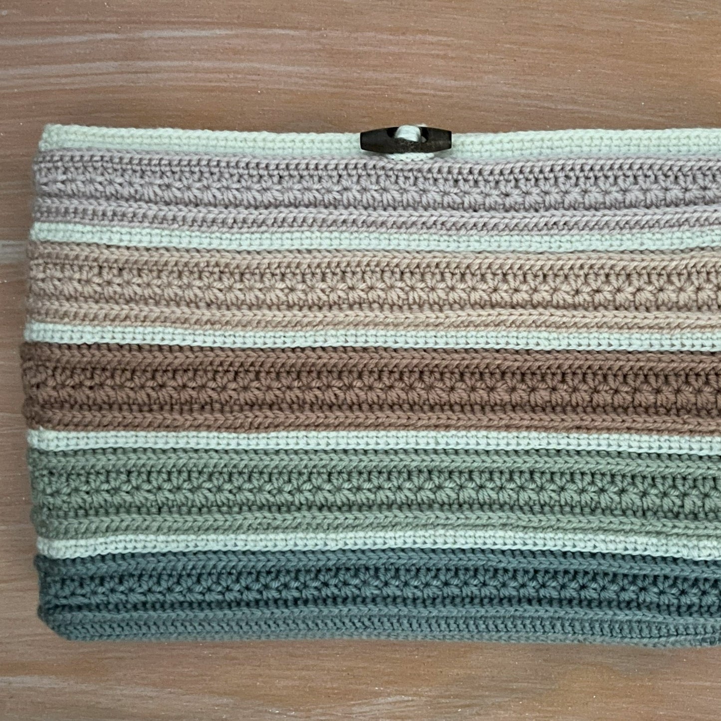 Crocheted clutch bag with striped pattern on a wooden surface