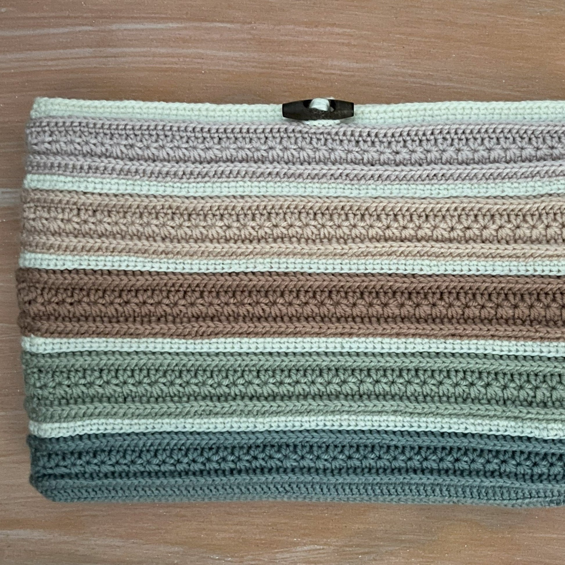 Crocheted clutch bag with striped pattern on a wooden surface