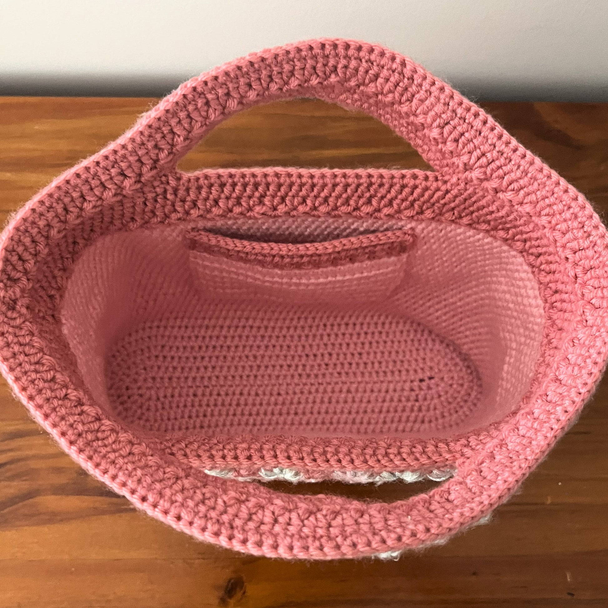 Pink crocheted basket on a wooden surface