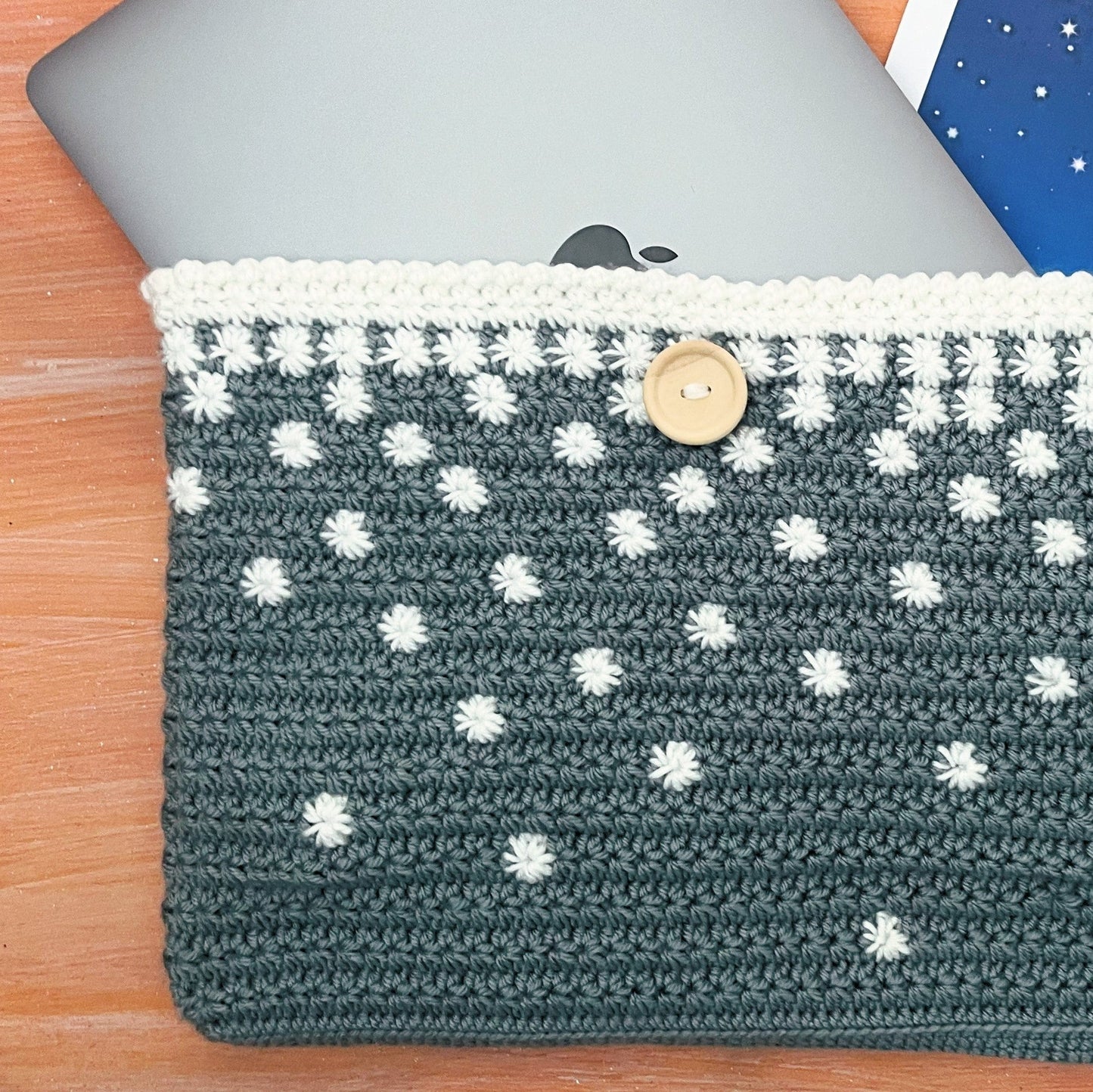 Crocheted pouch with a laptop on a wooden surface with a mug and photo frame.