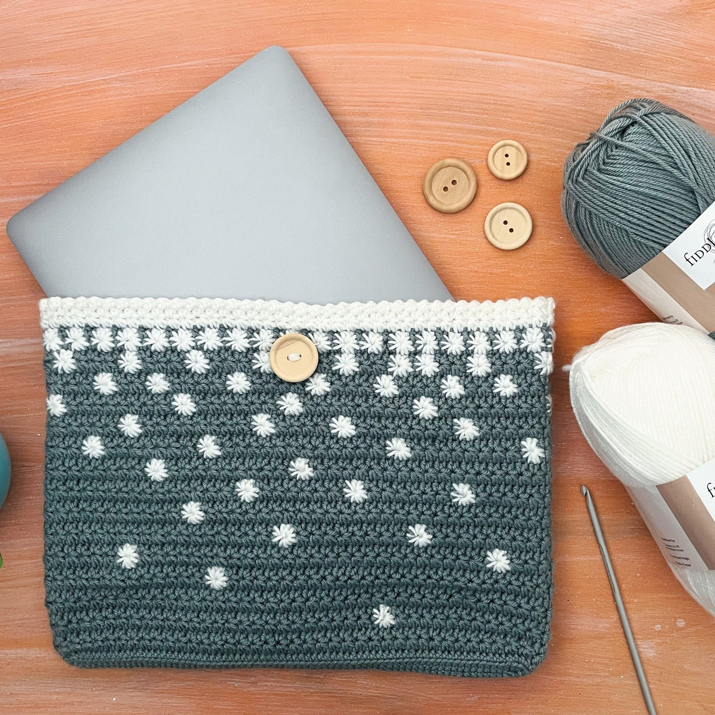 Crocheted pouch with polka dot pattern on a wooden surface with yarn and buttons.