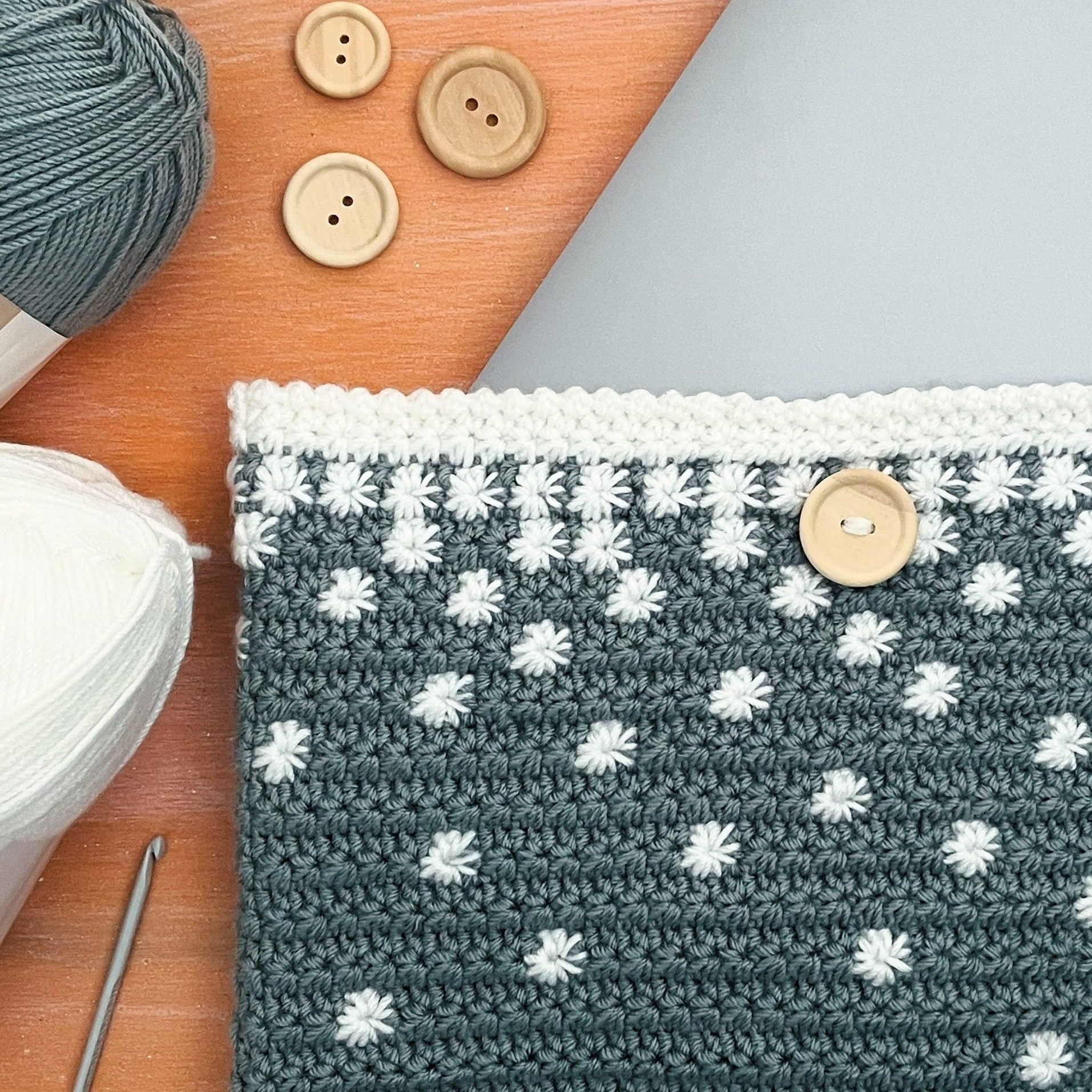 Crocheted pouch with falling stars pattern on a wooden surface with yarn and buttons.