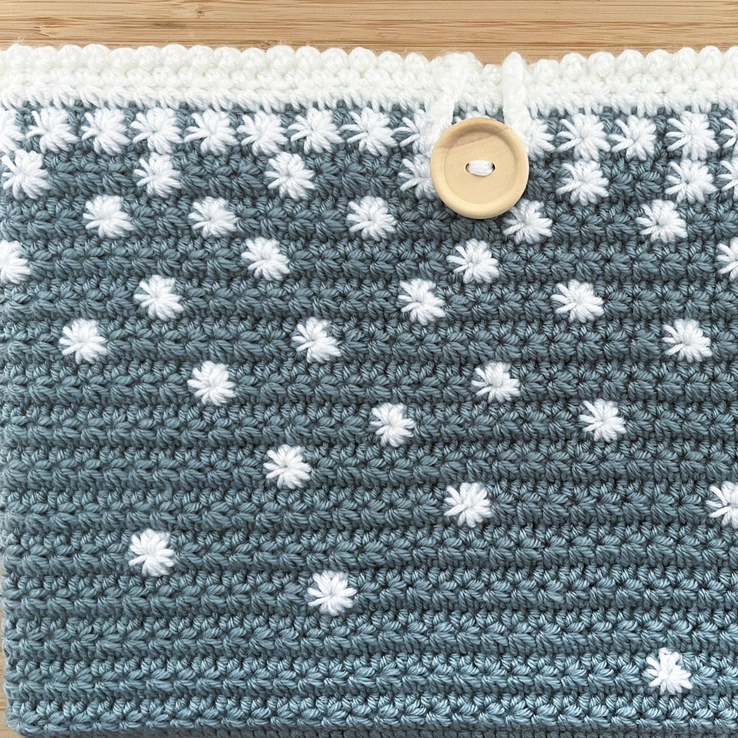 Crocheted pouch with white flower patterns on a wooden surface