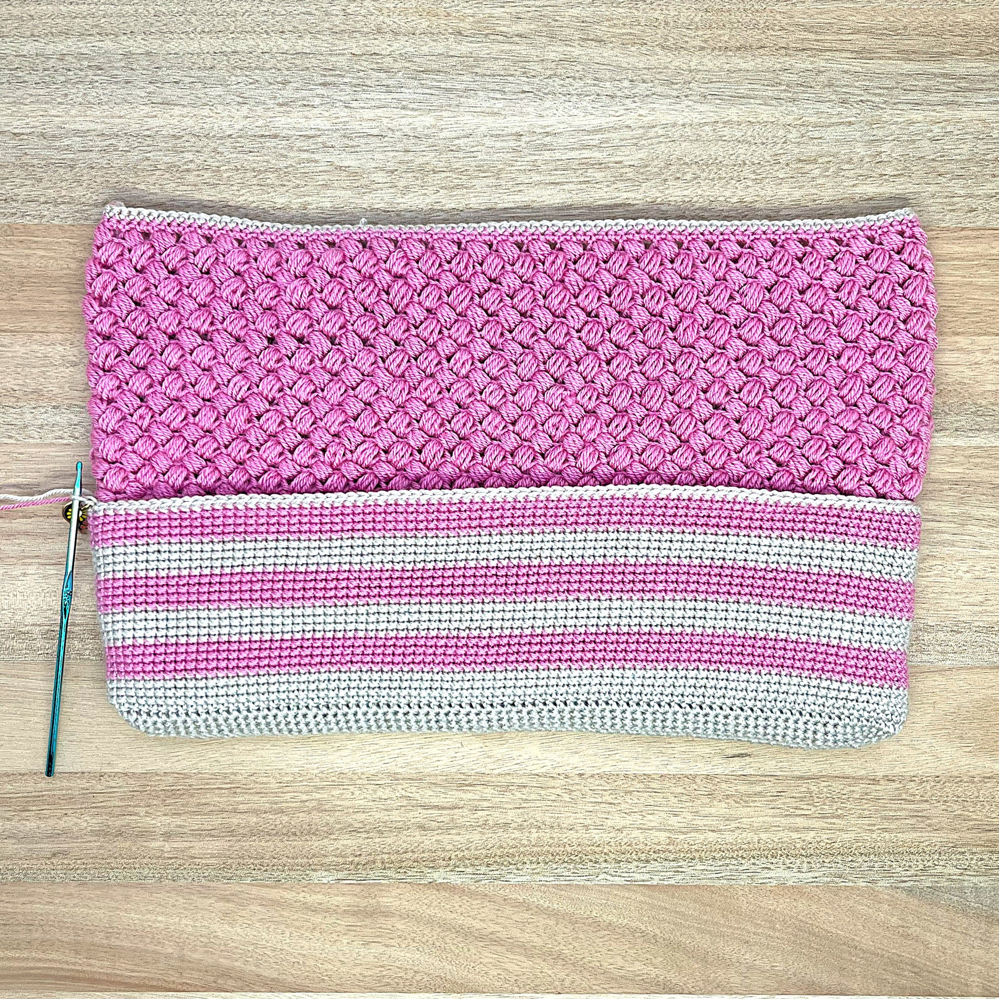 Pink crochet lined pouch with a white stripe on a wooden surface