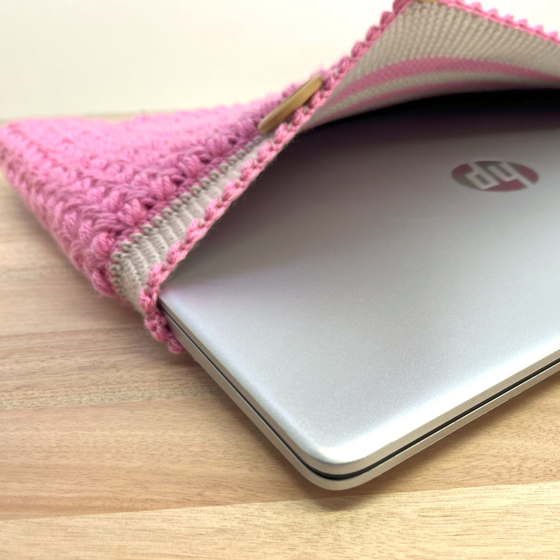 Silver HP laptop in a pink and beige fabric sleeve on a wooden surface