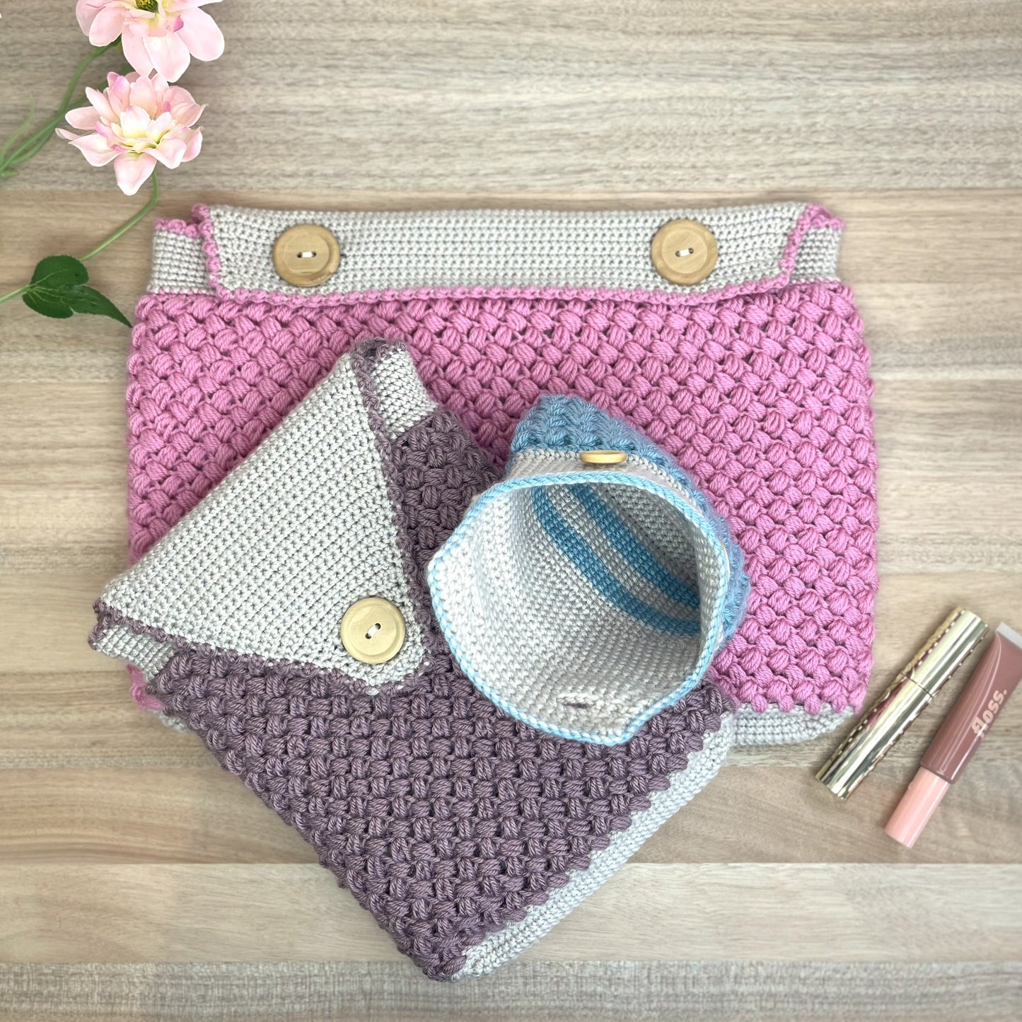 Two crocheted bags on a wooden surface with flowers and lipsticks.