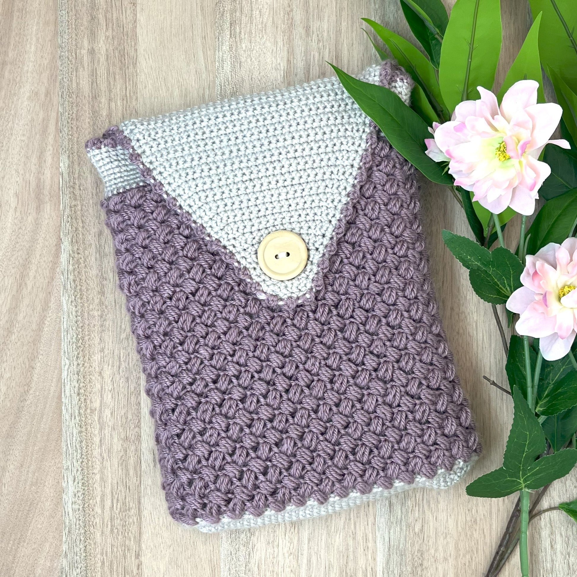 Handmade crochet pouch with a button on a wooden surface with flowers.