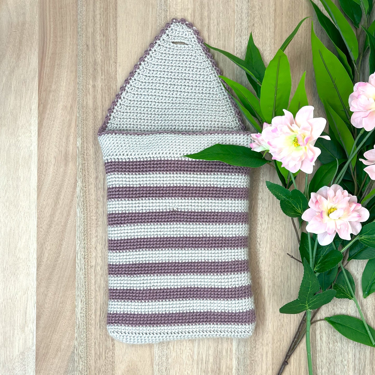 Striped knitted pouch on a wooden surface with flowers and leaves.