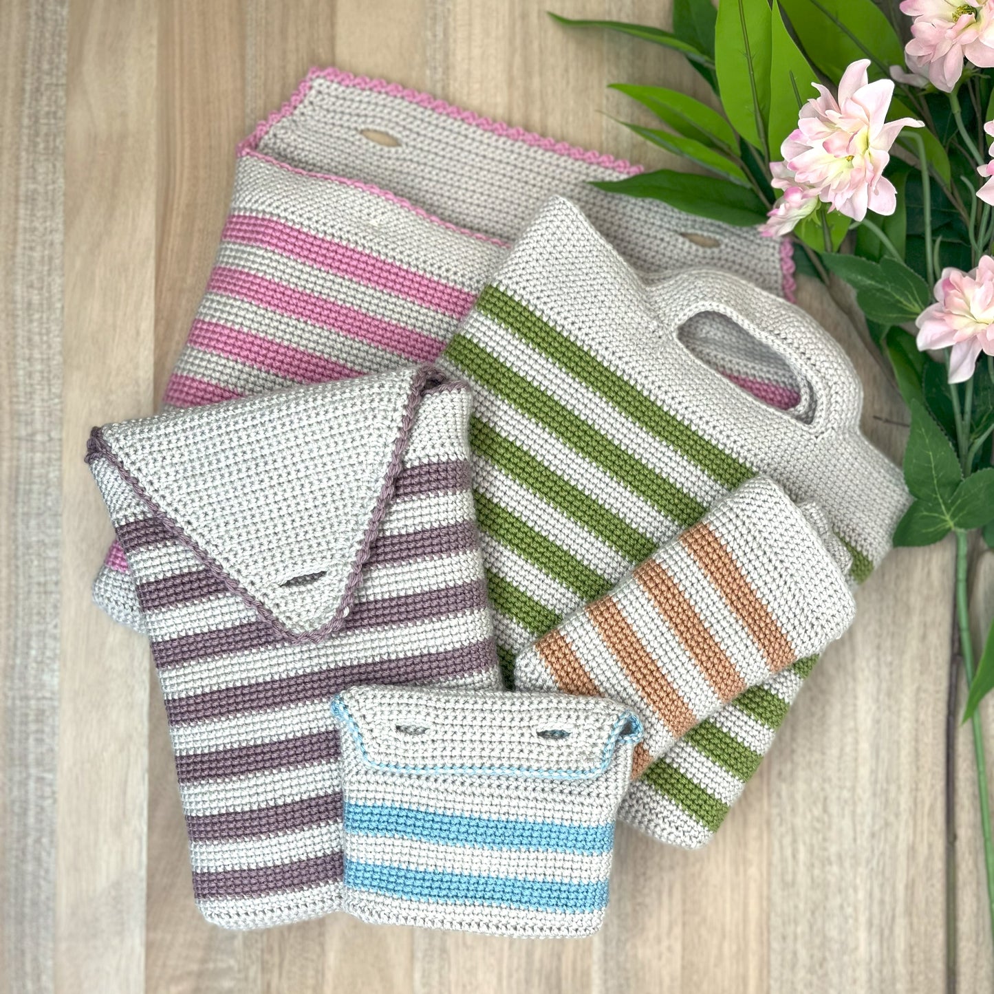 Set of crocheted bags with striped patterns on a wooden surface with flowers.