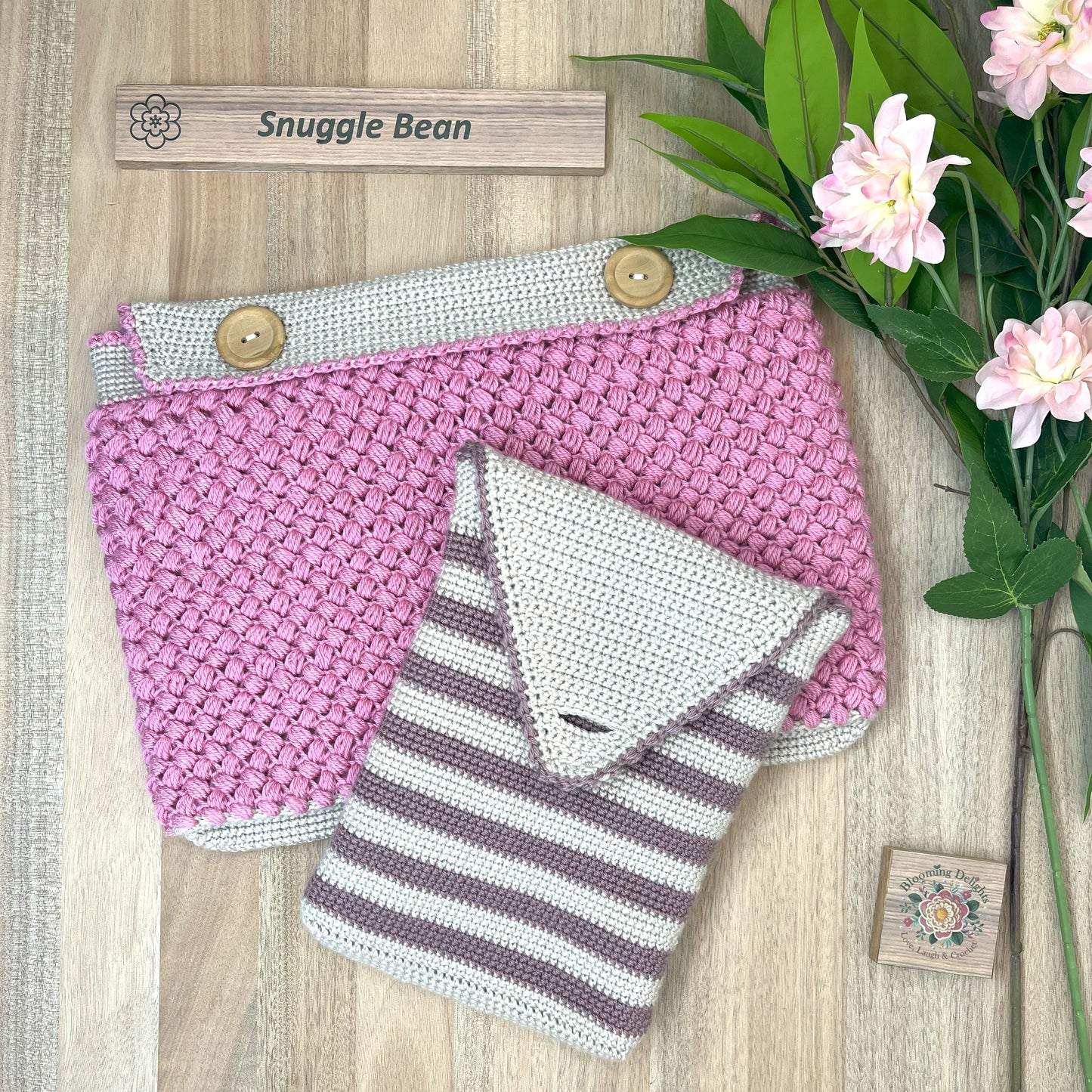 Knitted snuggle bean crochet pouch with pink and white pattern on a wooden surface with flowers.