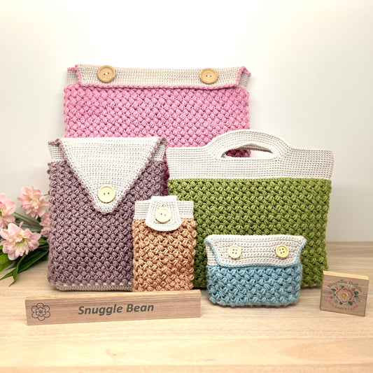 Set of crocheted bags in various colors with 'Snuggle Bean' branding on a wooden stand.