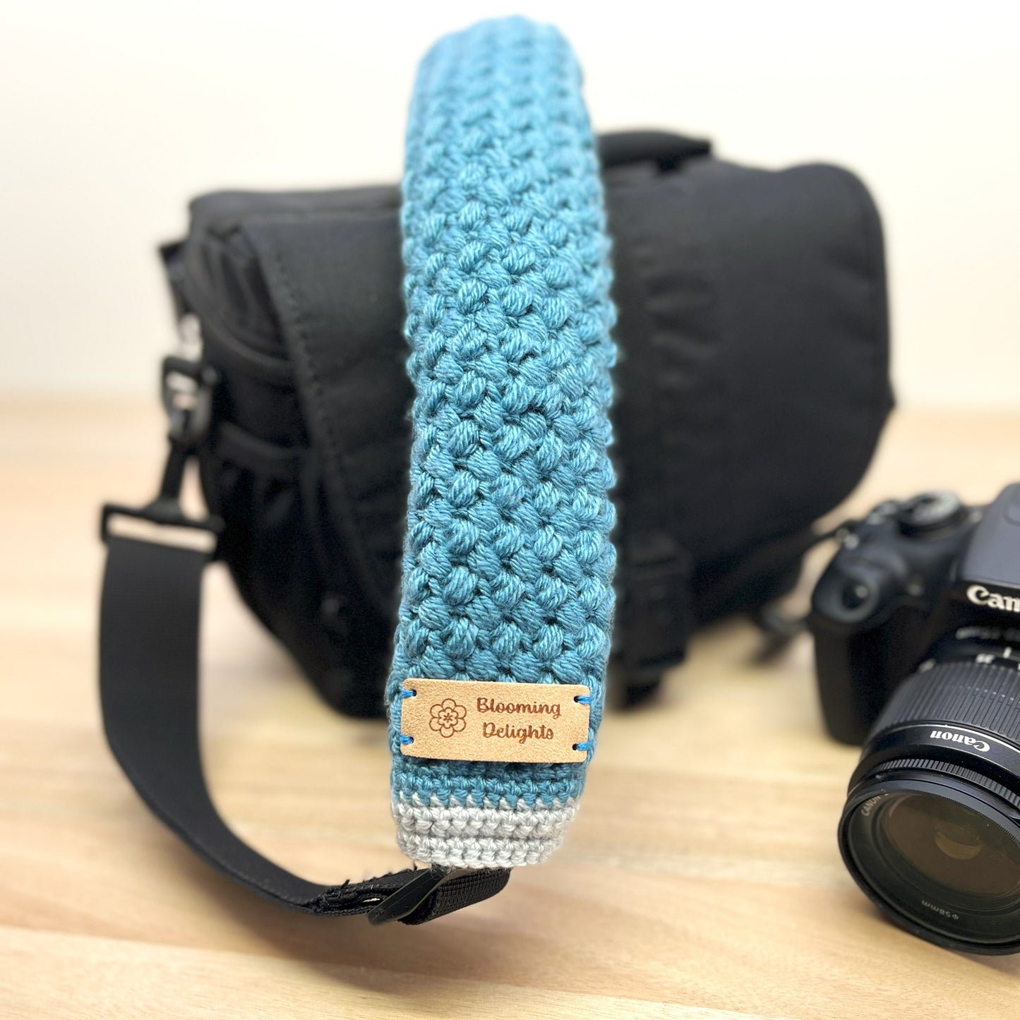 Camera with a blue textured strap and 'Blooming Delights' label on a wooden surface