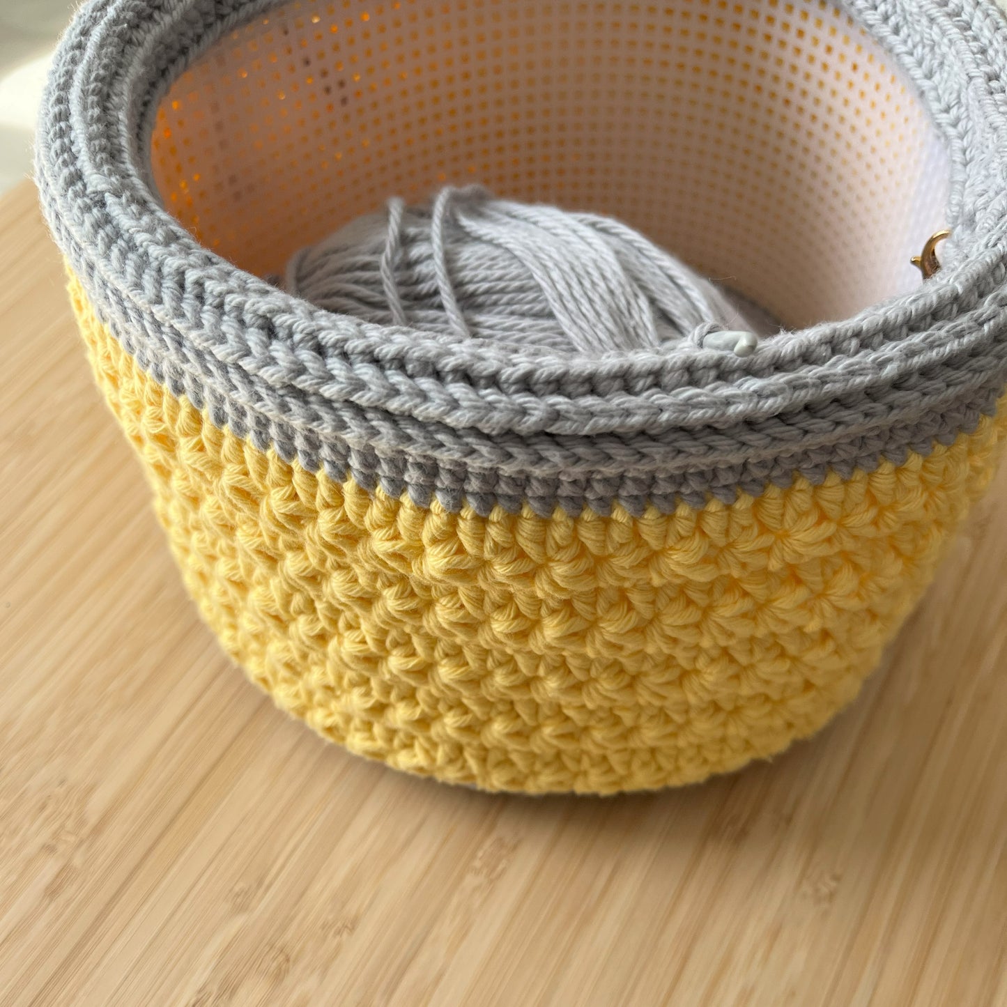 Crocheted yellow and gray basket on a wooden surface