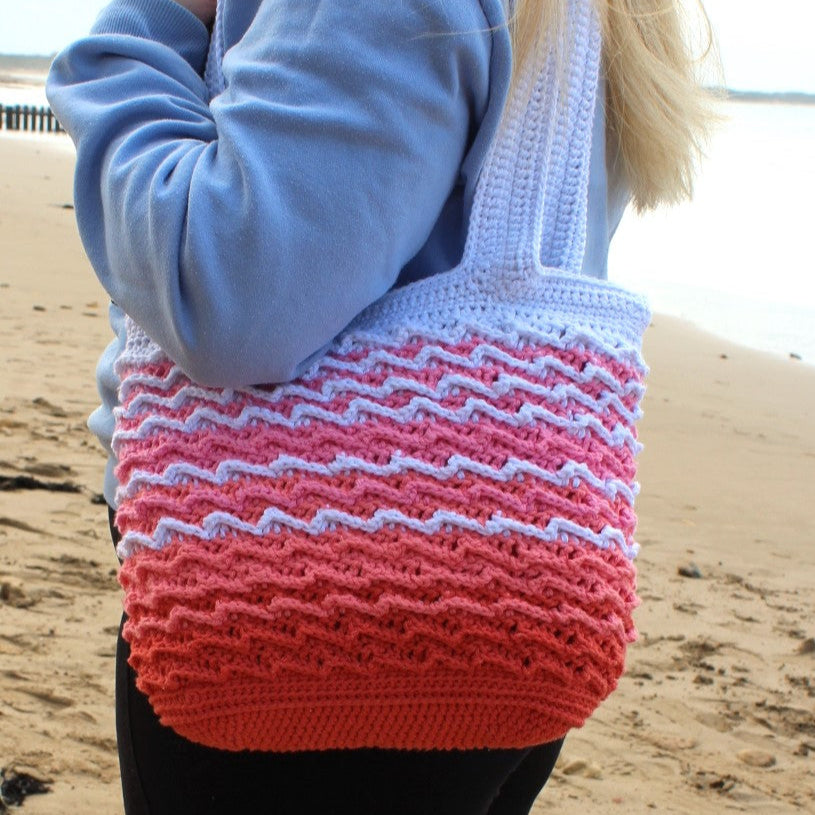 Person holding a colorful woven bag on a beach