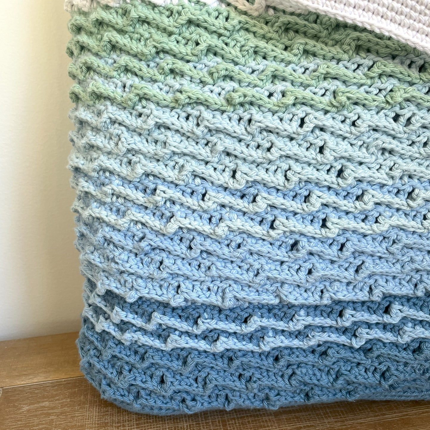 Stack of crocheted fabric pieces in green, blue, and beige on a wooden surface.