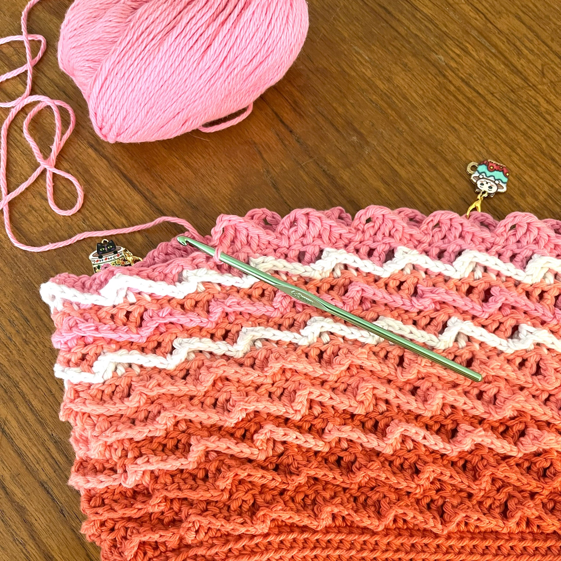 Crocheted fabric with pink yarn and crochet hook on a wooden surface