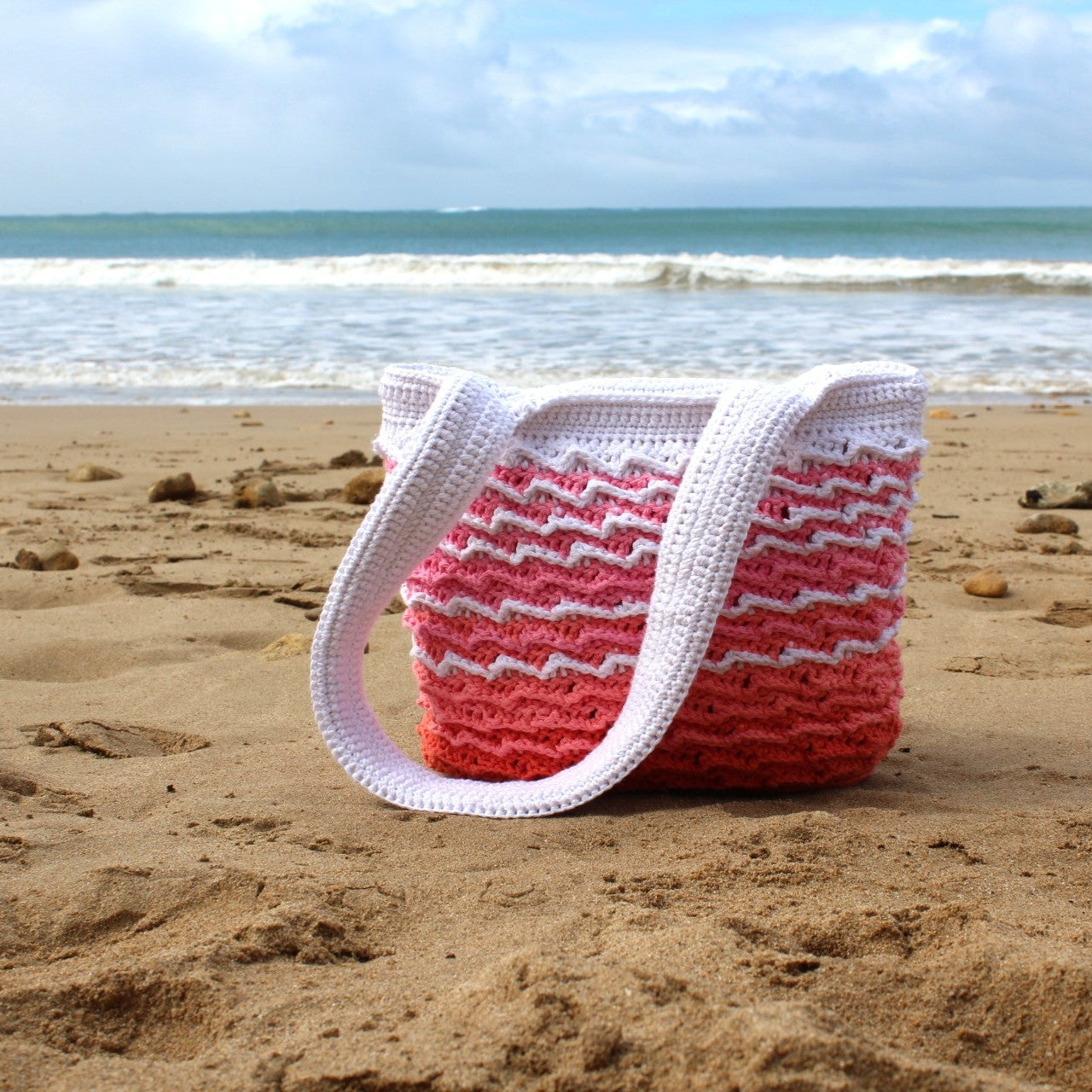 Pink and white striped bag on a sandy beach with ocean waves in the background
