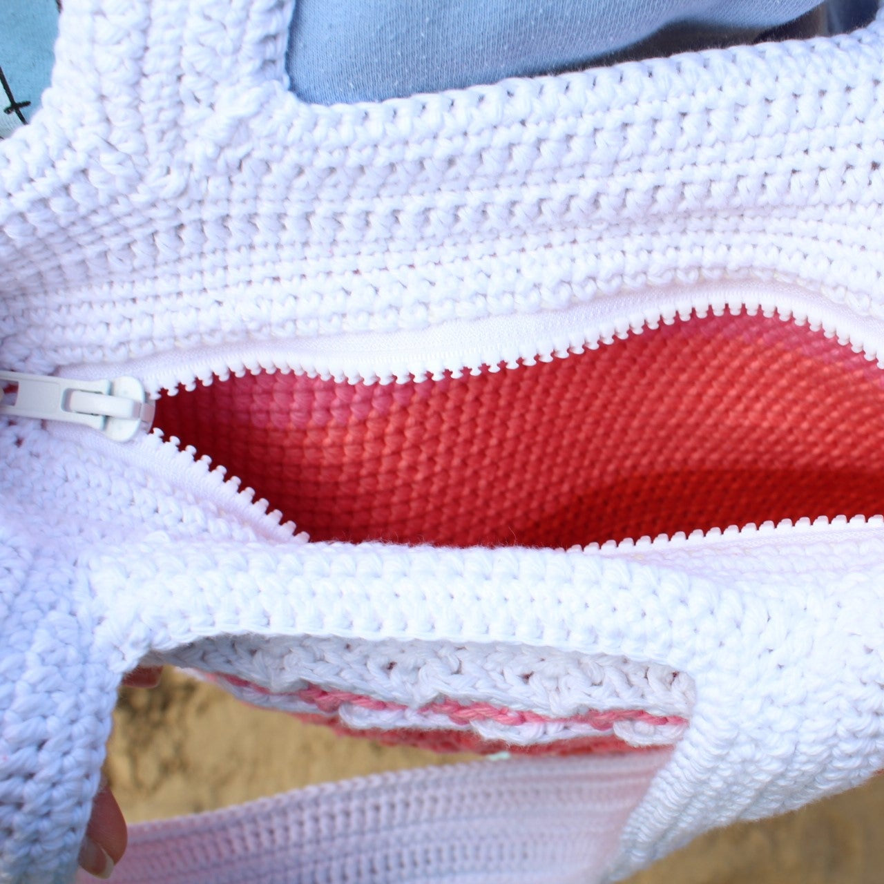 Close-up of a crochet handbag with a red crochet interior and a zipper being adjusted by a hand.