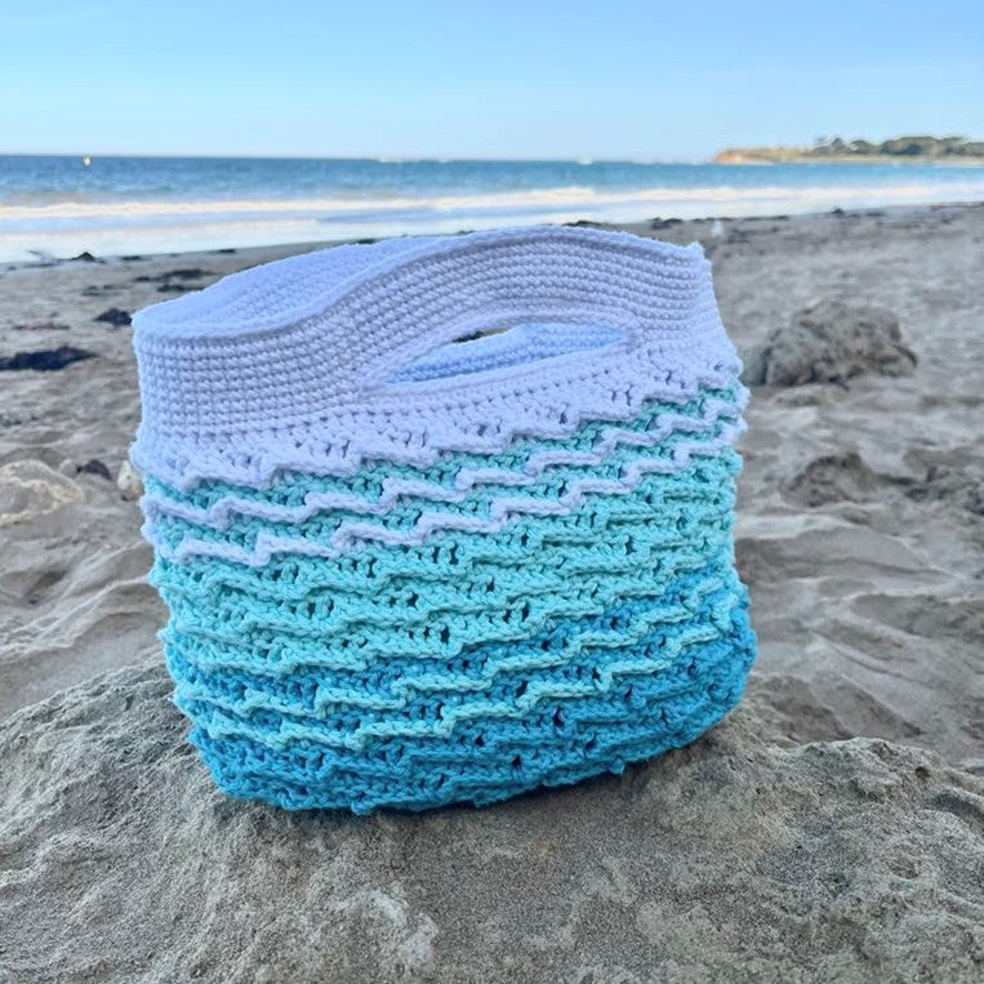 Blue and white woven bag on a beach with ocean in the background
